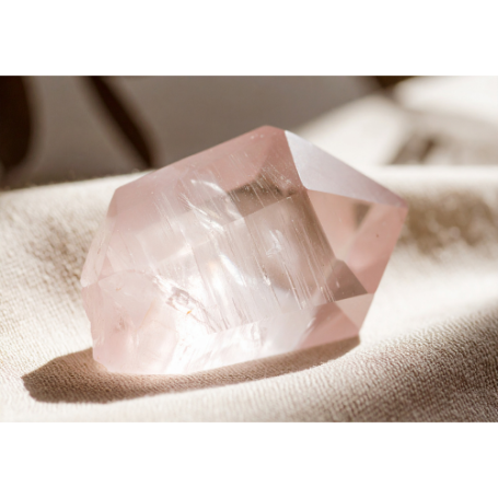 Rosa Quarzstein auf einem weichen Untergrund liegend, mit klarer, transparenter Struktur.